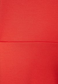 Punainen, teksturoitu kangas, jossa on sileä pinta, näyttää hieman tummemman vaakasauman keskellä. Pehmeä, venyvä materiaali.
