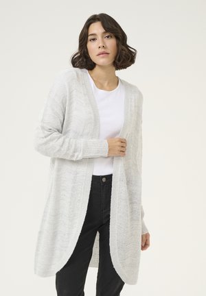 Cardigan lung tricotat de culoare gri deschis, cu front deschis, model texturat și manșete cu nervuri, purtat peste un tricou alb și blugi negri.