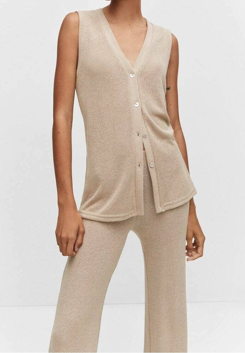 Haut beige sans manches à col en V avec boutons, associé à un pantalon large texturé assorti sur un mannequin debout.