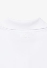 White collared shirt close-up showing embroidered logo detail on the upper back below the collar.