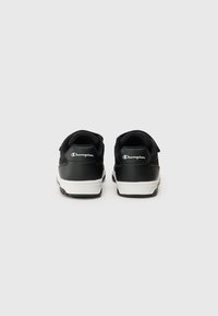 Des chaussures de sport noires avec une tige en cuir lisse, des panneaux en mesh, une semelle blanche et des accents de logo sur le talon. Équipées de sangles réglables.
