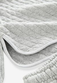 Harmaa tilkkutäkki, jossa on herringbone-kuvio, pehmeä rakenne ja valkoinen reunus.