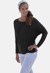 Schwarzes, lässig geschnittenes Langarmoberteil mit weitem Ausschnitt, aus weicher Textur. Kombiniert mit hellblauen Jeans. Keine auffälligen Muster oder Akzente.