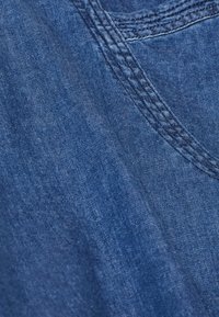 Tummansininen denim-kangas, jossa on hieman kulunut rakenne. Kulkureunoilla näkyvä ompelu ja sileä pinta hienovaraisella sävytyksellä.