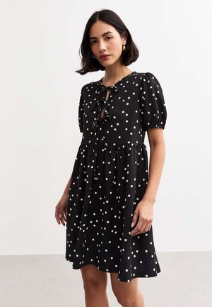 Vestido negro con lunares, con mangas cortas abullonadas, que presenta un cierre con cinta en el cuello y un dobladillo acampanado. Fabricado en tejido texturizado.