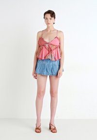Top senza maniche di colore rosa con motivo a fantasia e volant, abbinato a una minigonna di jeans. La modella indossa sandali marroni con lacci e grandi orecchini a cerchio.