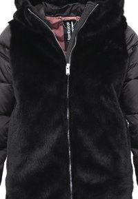 Giacca in pelliccia sintetica nera con chiusura a zip, cappuccio e maniche in tessuto a contrasto. L'interno è foderato con un morbido tessuto bordeaux.