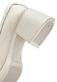 Zapato alto beige con un acabado mate texturizado. Presenta un tacón cuadrado grueso y blanco con detalles acanalados en la base.