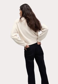 Pull en tricot crème avec une finition texturée, présentant des épaules tombantes et des poignets côtelés, associé à un pantalon noir taille haute.