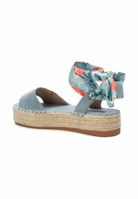 Sandalia espadrille de ante azul con suela de yute trenzado y un lazo de tela con patrón floral alrededor del tobillo para añadir un detalle adicional.