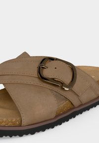 Μπεζ σουέτ σανδάλι με φαρδιές επικαλυπτόμενες λουρίδες, αγκράφα σε χρυσό τόνο, φελλό πάτο και μαύρη υφασμένη καουτσούκ σόλα.