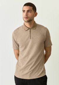 Camisa polo de manga corta beige con un patrón de cuadros texturizado, cuello y cremallera de cuarto. Fabricada con tela liviana.