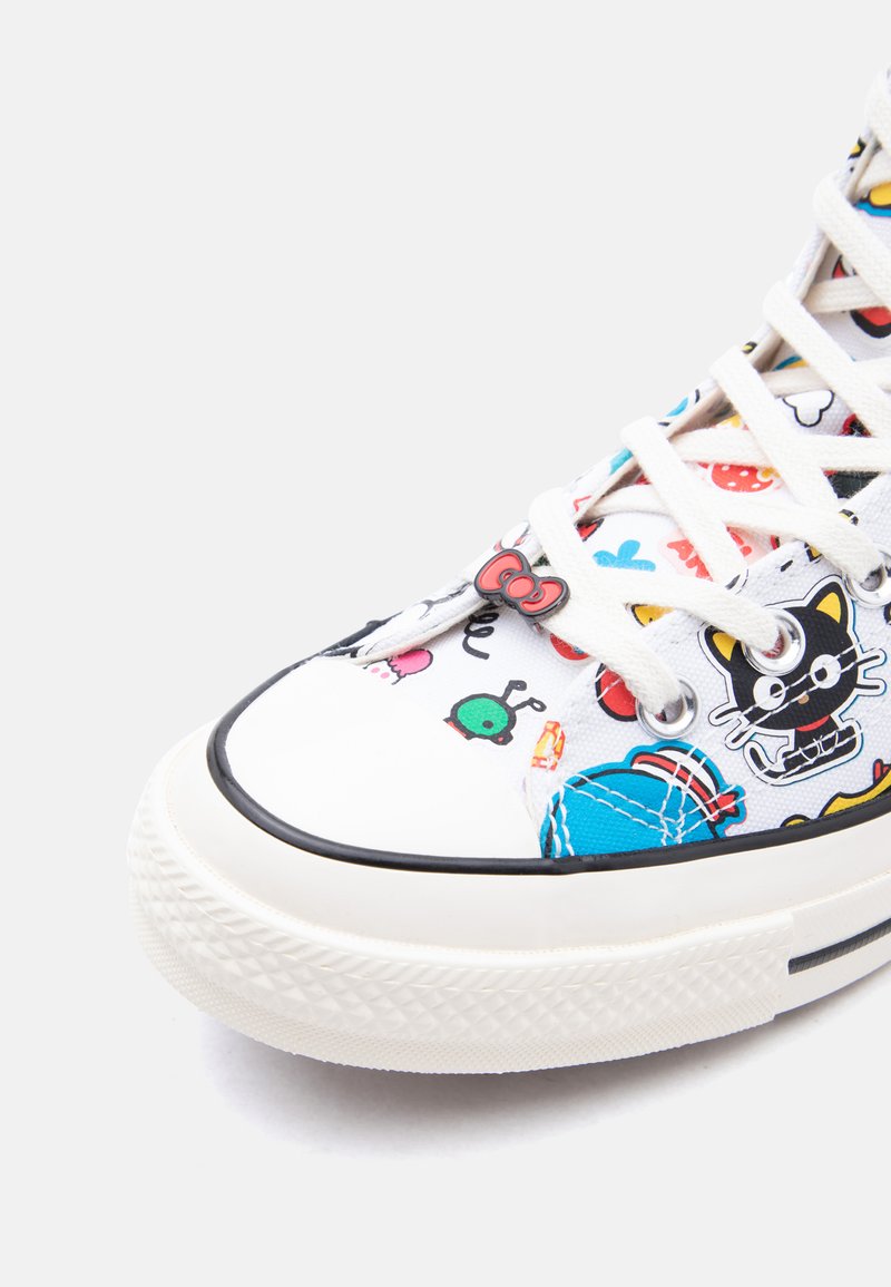 Zapatilla blanca con personajes de dibujos animados coloridos, incluyendo un gato negro con gafas y un adorno de lazo rojo en la zona de la puntera.