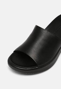 Sandale noire à enfiler, à bout ouvert, avec une large lanière en cuir et une semelle rembourrée, présentée sur un fond blanc.