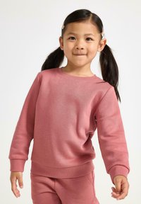 Felpa rosa realizzata in morbido tessuto, con scollatura rotonda, polsini a costine e vestibilità rilassata. Abbinata a pantaloni coordinati.