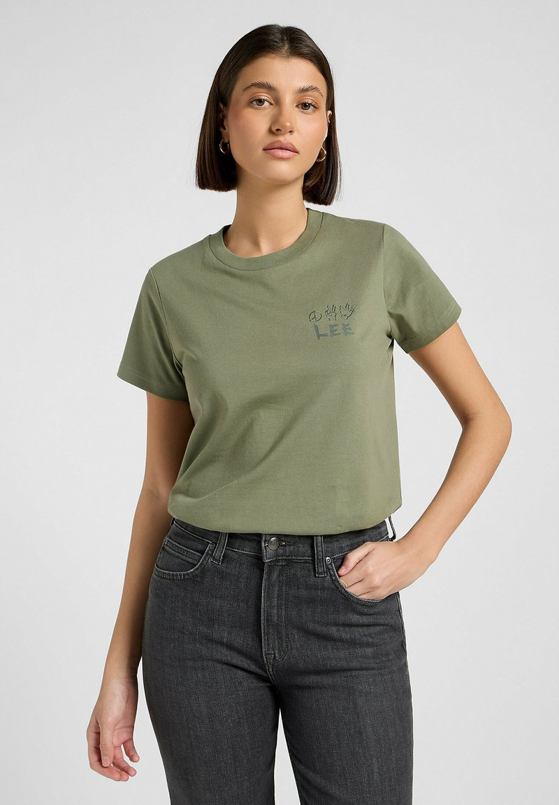 Olchowa zielona bawełniana koszulka z okrągłym dekoltem, krótkim rękawem i nadrukowanym logo "LEE" na lewej piersi. W zestawie z ciemnoniebieskimi dżinsami.