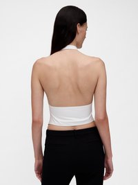 Baltas halterio stiliaus trumpas viršus su lygiu audiniu, prigludęs siluetas, atvira nugara, derinamas su prigludusiomis juodomis kelnėmis su juosmens juostele ir kišenėmis.