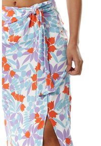 Floral wrap skirt in white, featuring red tulips and light blue leaves. Knot detail at waist and side slit for added design. Soft texture.