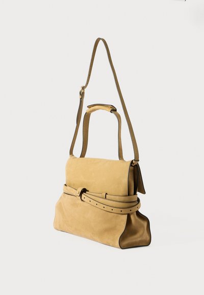 Zachte tan suede handtas met een bovenhandvat, verstelbare schouderband en een brede riemdetail rond het lichaam op een effen achtergrond.