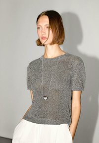 Gray knitted short-sleeve top with a relaxed fit, featuring a round neckline and detailed texture, paired with a long silver necklace.