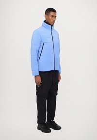 Light blue puffer jacket with a high collar, front zipper, and black accents, paired with black cargo pants and black sneakers.