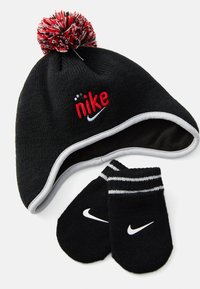 Cappello in maglia nera per l'inverno con pompon rosso e bianco e logo Nike rosso, abbinato a guanti neri Nike con swoosh bianco e polsini a righe.
