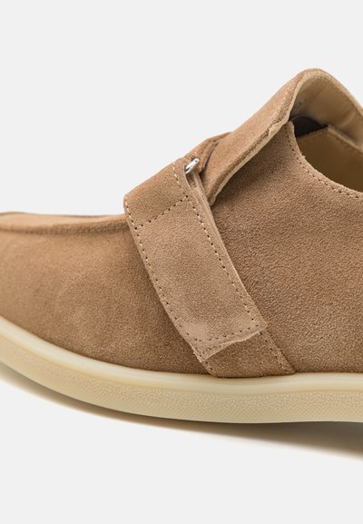 Chaussure en daim brun avec un bout rond et une fermeture par sangle, dotée d'une semelle en caoutchouc crème et d'un dessus texturé pour une meilleure adhérence.