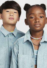 Du vaikai vilki atitinkančius šviesiai mėlynus kordūrinius marškinėlius su mygtukų užsegimu. Mergaitė turi karoliukų vėrinį, o berniukas po marškiniais turi geltoną marškinėlį.