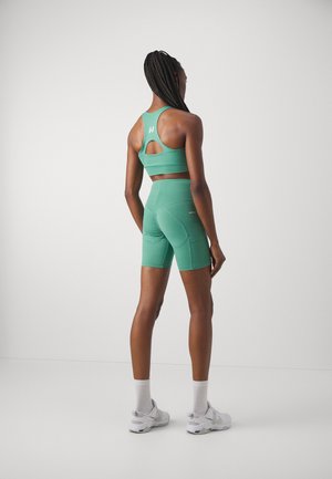 Green sports bra and matching high-waisted shorts, made of sleek fabric, featuring a cutout detail at the back and stitched accents.