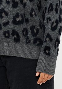 Sweater cinza com manchas de leopardo pretas, apresentando uma textura macia e punhos canelados. Acentos de fio metálico visíveis na malha.
