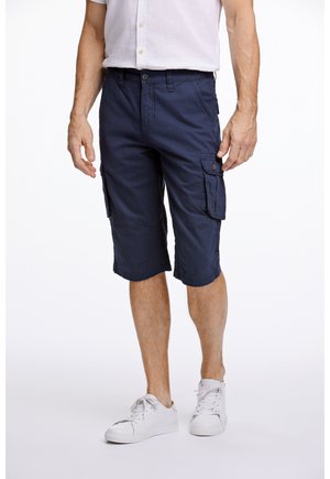 Marine Cargo-Shorts mit knielangem Design, aus Baumwolle gefertigt. Verfügt über Seitentaschen und einen Knopfverschluss. Kombiniert mit weißen Sneakers.