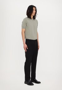 Kortermet, lysegrønn strikket skjorte kombinert med svarte, skreddersydde bukser og svarte loafers. Minimalistisk design med en avslappet passform.