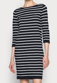 Robe rayée avec des rayures horizontales bleu marine et blanches, manches trois-quarts, encolure ronde, et un petit logo sur la poitrine. Tissu lisse.