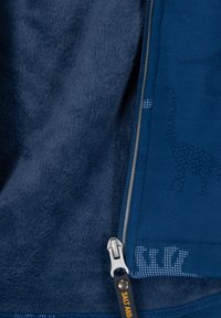 Marineblauwe jas met een zachte fleece voering, een rits met een zilveren trekker en subtiele dinosaurustexturen op de buitenstof.