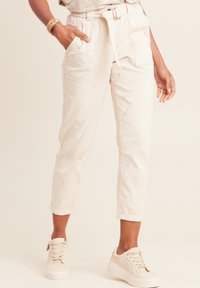 Beige katoenen broek met een drawstring tailleband, opgerolde manchetten en zijzakken, gecombineerd met lichte sneakers. Getextureerde stof.