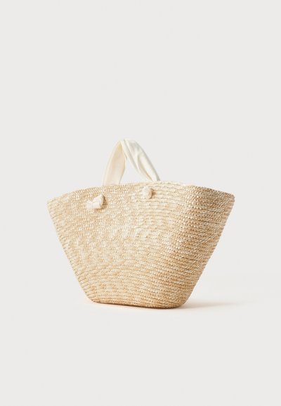 Sac cabas tissé en paille naturelle avec des poignées courtes en tissu crème nouées en nœuds sur un fond clair uni.