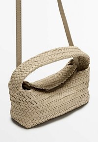 Beżowa pleciona torba na ramię z zakrzywionym uchwytem u góry, teksturowanym wykończeniem i cienkim paskiem na ramię. Klapka zamykająca zasłania otwarcie.