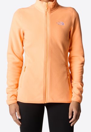 Veste en polaire orange clair à fermeture éclair avec poches latérales portée par une personne, avec un petit logo sur le côté gauche de la poitrine.