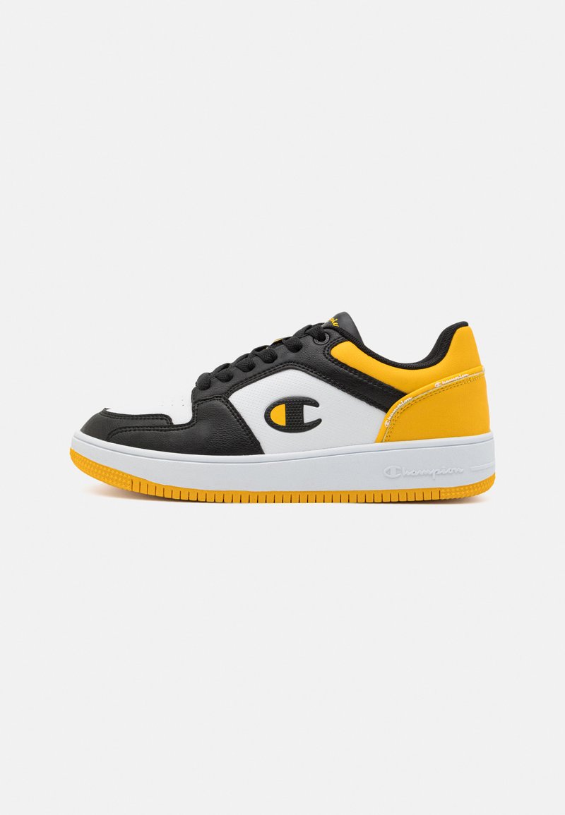 Adidași negri, albi și galbeni cu un superior din piele și talpă din cauciuc. Au un vârf rotunjit, un design cu șireturi și un detaliu proeminent al logo-ului.