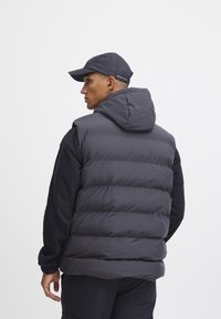 Temno siva pufasta jopica s kapuco, z nastavljeno prešano zasnovo, v kombinaciji z dolgimi rokavi črnim flisastim majico in ujemajočo se kapo.