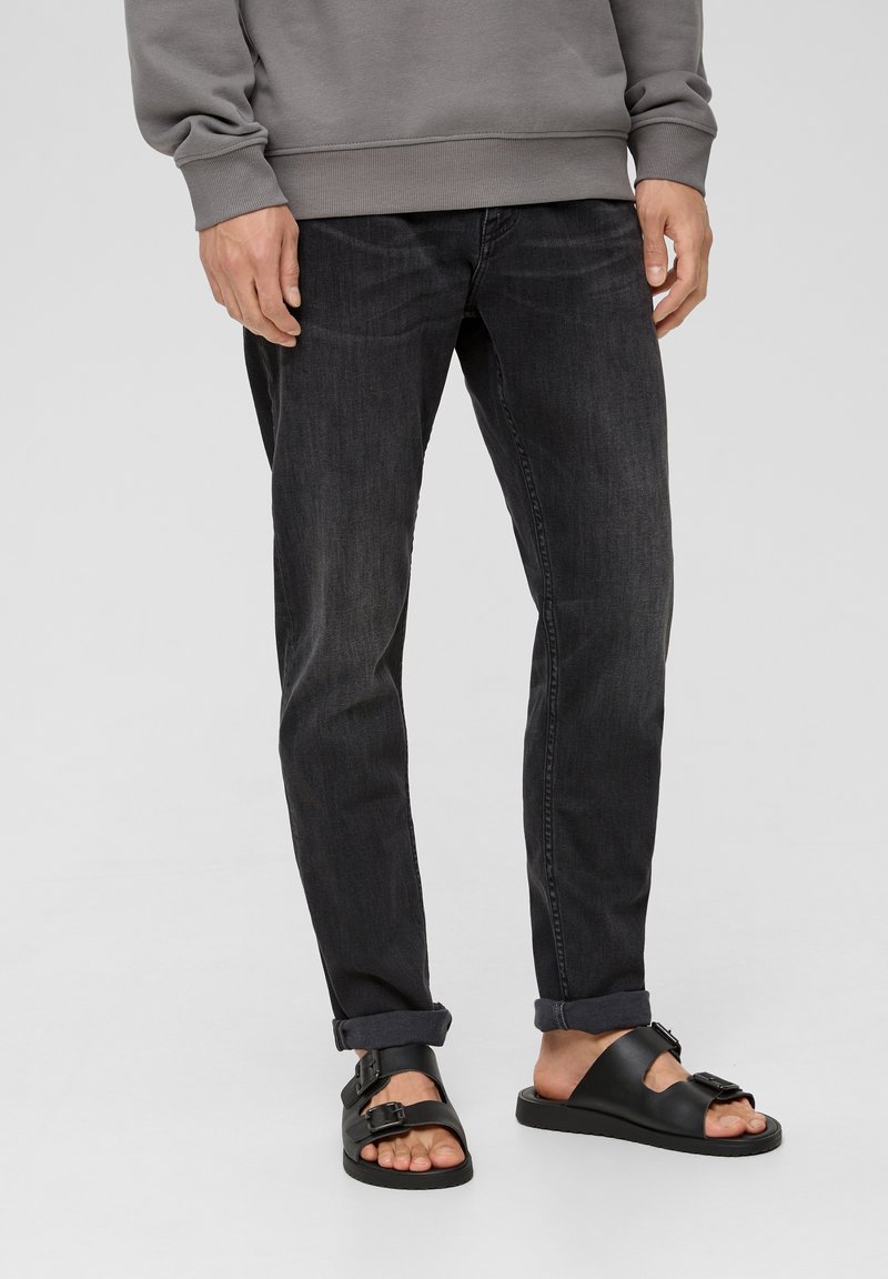 Dark denim jeans with a straight fit, featuring a subtle wash. Paired with black sandals, highlighting a buckle detail and flat sole.