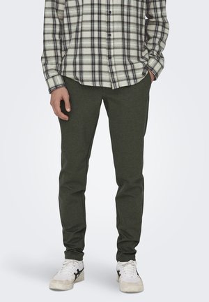 Groene, slim-fit broek gemaakt van zachte stof, gecombineerd met een geruite button-up shirt. Witte sneakers met zwarte accenten maken de look af.
