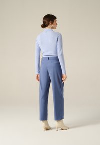 Maglione azzurro chiaro a coste con collo alto, abbinato a pantaloni blu su misura e stivaletti beige alla caviglia. Design minimalista, senza fantasia.