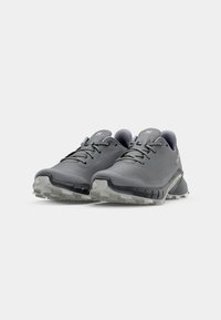 Chaussures de course grises avec une tige en mesh, un bout arrondi, des lacets, une semelle intermédiaire rembourrée et une semelle extérieure en caoutchouc texturé. Les accents incluent un logo réfléchissant.