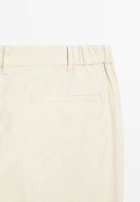 Pantalon en lin beige avec une taille élastique, détail de poche arrière, et une texture lisse, partiellement visible de la taille vers le bas.