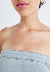 Ανοιχτό μπλε τζιν τοπ χωρίς ιμάντες με λεία υφή και ελάχιστη ραφή. Κοντινή λήψη του ντεκολτέ και της άνω περιοχής του στήθους.