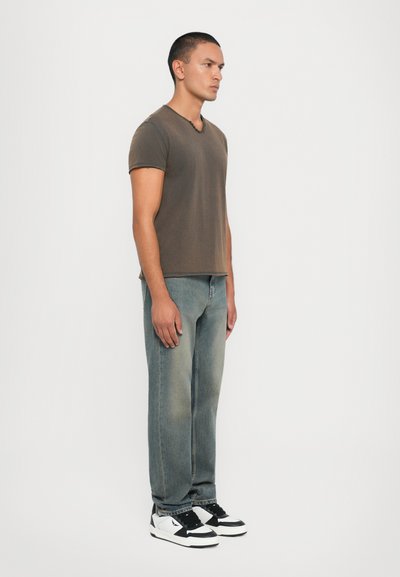 Brown cotton t-shirt, soft texture, short sleeves; faded blue denim jeans with a loose fit; black and white sneakers with contrasting accents.