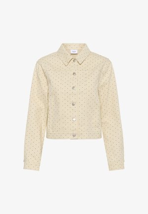 Bēša īss jaka ar melniem punktiņiem, sudraba spiedpogām priekšpusē, garām piedurknēm un asimetrisku apkakli.