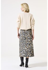 Beige Oversized-Pullover mit strukturiertem Strick, kombiniert mit einem knielangen Leopardenmusterrock. Schwarze kniehohe Stiefel vervollständigen das Outfit.
