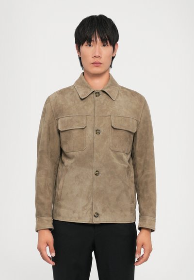 Chaqueta de ante marrón con cuello, dos bolsillos frontales, cierre de botones y mangas largas, llevada por un modelo sobre un fondo blanco.